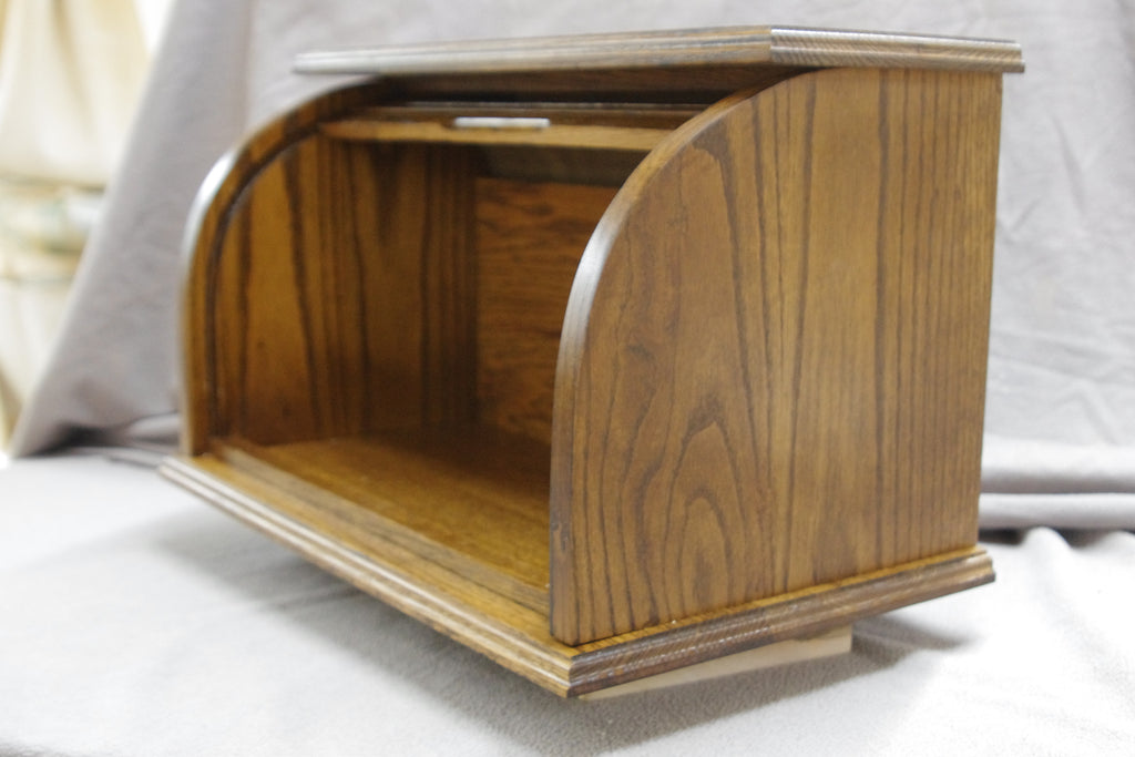 Oak bread box with a roll-top door, crafted from natural oak wood that beautifully highlights the grain. Stained in a darker shade of brown for a rich, inviting look, it offers a warm, rustic touch to any kitchen. The spacious interior helps keep bread and baked goods fresh, while the sturdy construction and classic design add both style and convenience. Shown from the front with the door fully open, showcasing its elegant design and practical functionality.