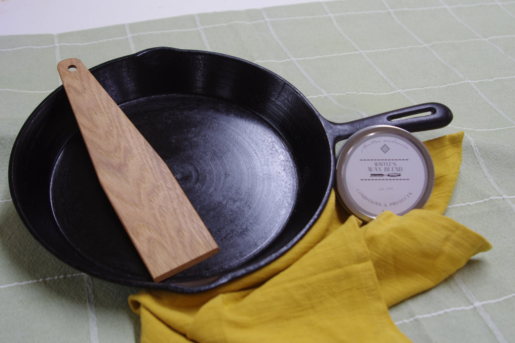 Black cast iron skillet with wooden spatula and yellow cloth 