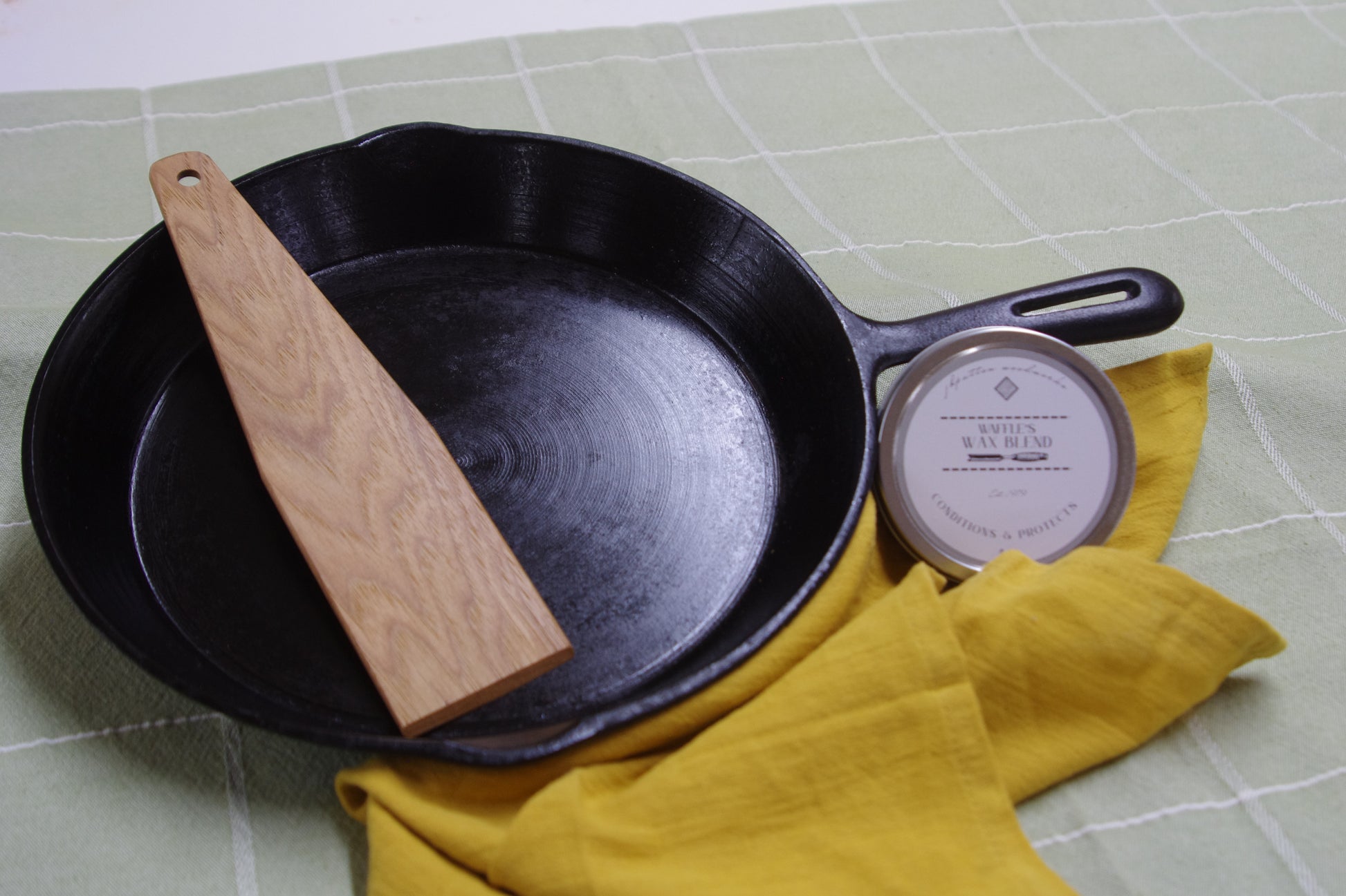 Black cast iron skillet with wooden spatula and yellow cloth 