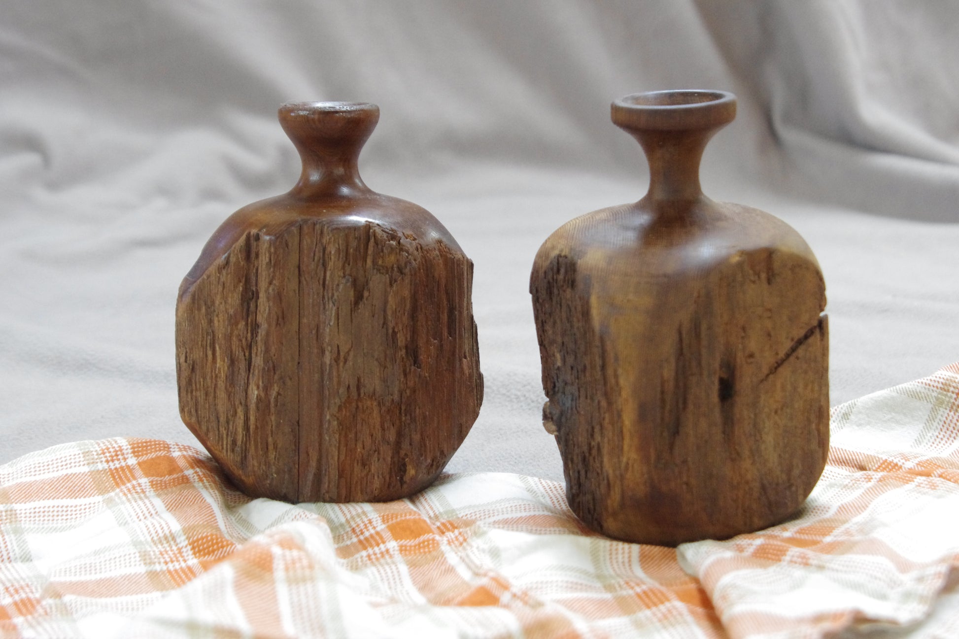 Two wooden vases on a plaid cloth with a neutral background