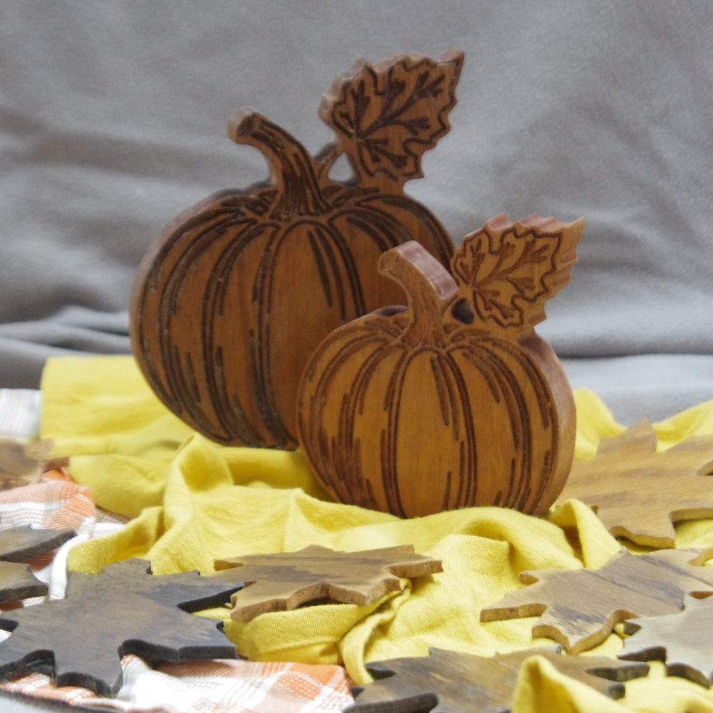 Wooden pumpkin and leaf decorations on a yellow cloth with a gray background