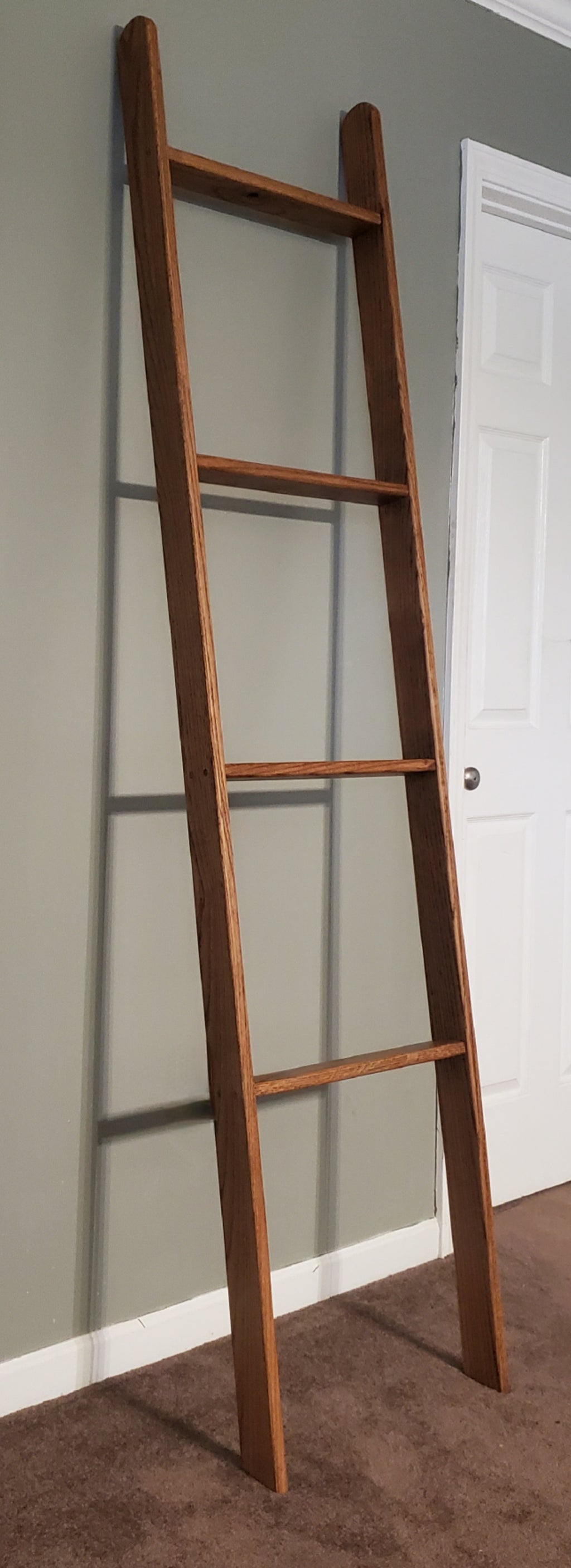 Wooden Oak Blanket Ladder leaning against a gray wall with a white door in the background.