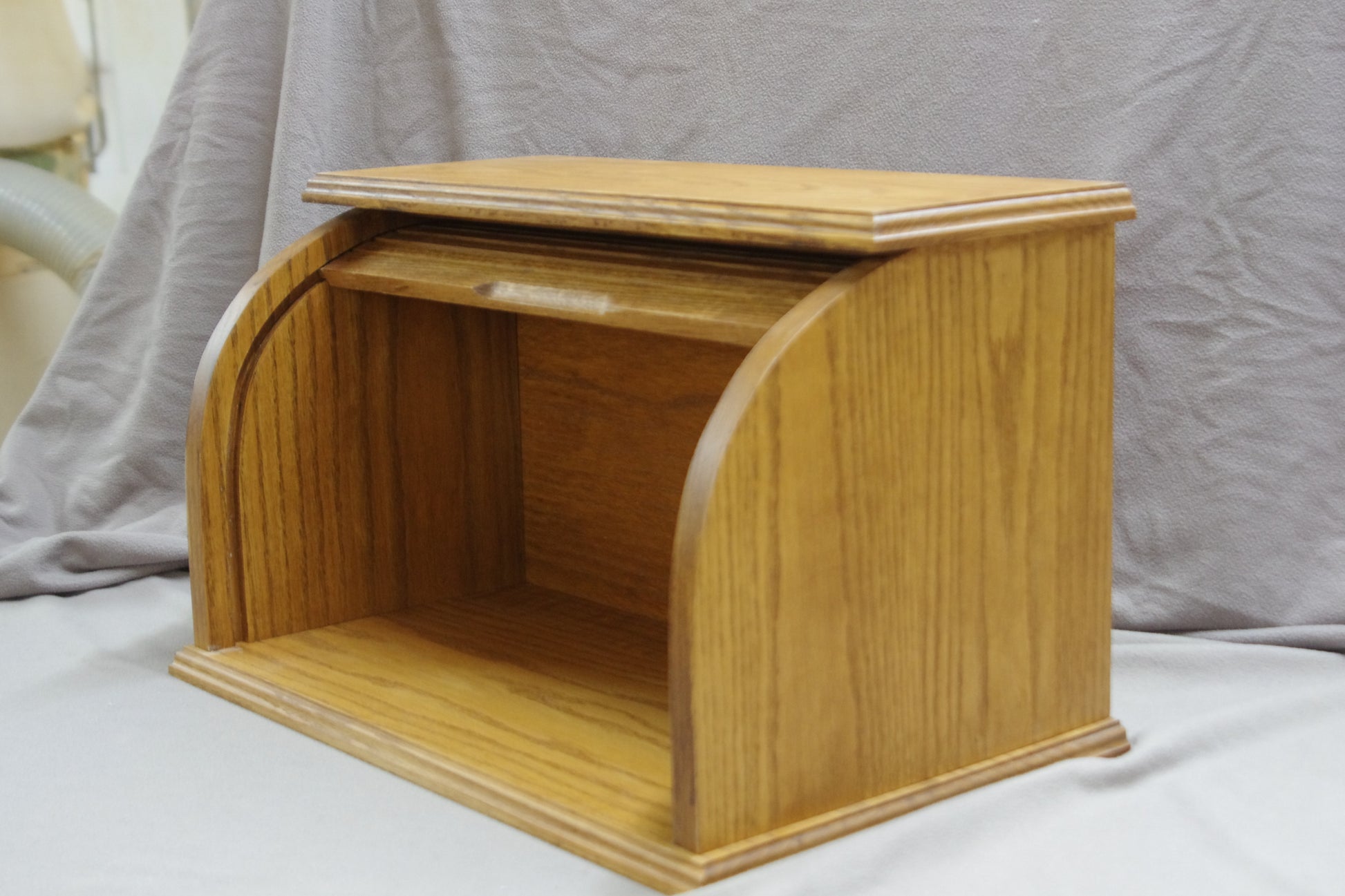 Oak bread box with a roll-top door, crafted from natural oak wood that beautifully highlights the grain. Stained in a light shade of brown for a rich, inviting look, it offers a warm, rustic touch to any kitchen. The spacious interior helps keep bread and baked goods fresh, while the sturdy construction and classic design add both style and convenience. Shown from the front with the door fully open, showcasing its elegant design and practical functionality.
Stain is Early American.