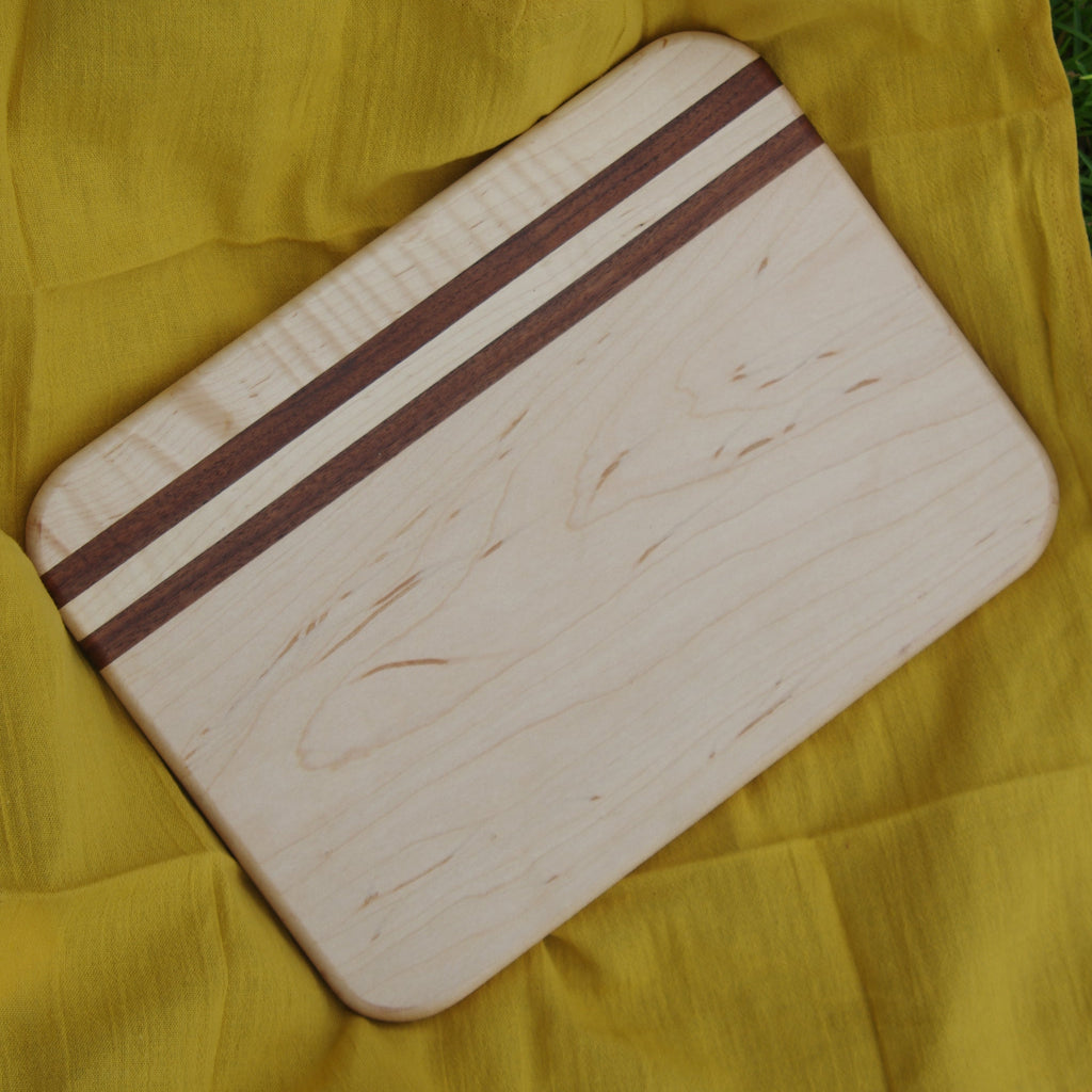 Wooden maple and walnut cutting board with a smooth, polished surface. The striking contrast between light maple and rich walnut wood adds a touch of elegance to any kitchen. Known for its durability, this board is perfect for chopping, slicing, and serving. Its natural wood grain and sleek design make it a timeless addition to your kitchen or a thoughtful gift for cooking enthusiasts.