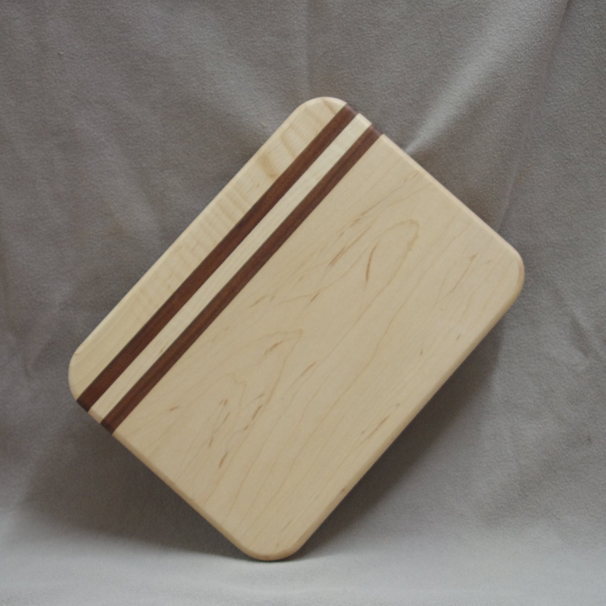Handcrafted maple wood cutting board with two rich walnut stripes, offering a sleek, modern design. The smooth, polished surface and durable construction make it perfect for chopping, slicing, and serving, adding both elegance and functionality to your kitchen.