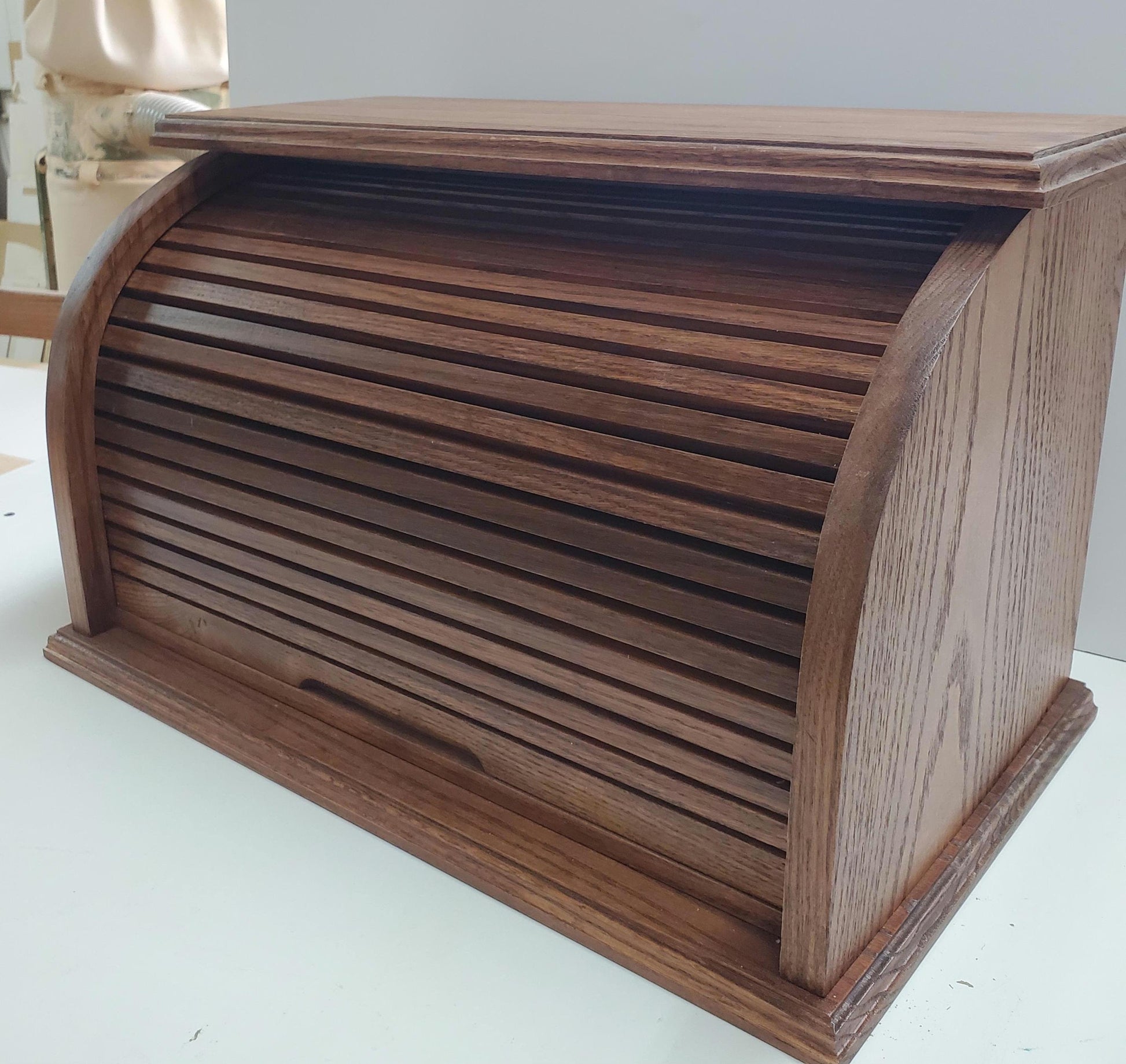 Front of Oak bread box with a roll-top door, crafted from natural oak wood that highlights its beautiful grain. Stained in a medium reddish-brown for a rich, inviting look, this bread box adds a warm, rustic touch to your kitchen. The spacious interior helps keep bread and baked goods fresh, while the sturdy construction and classic design offer both style and functionality. A perfect storage solution for keeping bread and other baked goods organized and fresh.
