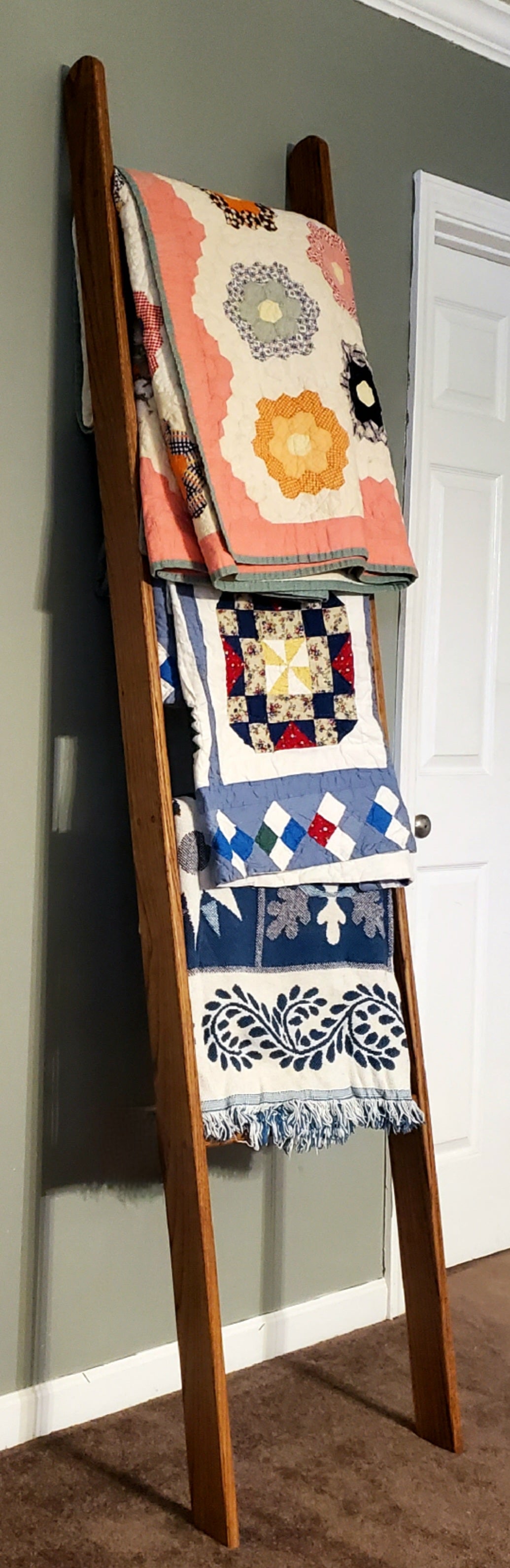 Wooden oak blanket ladder in a rich Early American stain, leaning gracefully against a plain wall with colorful quilts draped over it. This sturdy ladder combines style and functionality. Whether used in a living room, bedroom, or library, it adds a charming, vintage flair to your home décor. Ideal for organizing or showcasing your favorite quilts, this blanket ladder also serves as a unique, space-saving storage solution.