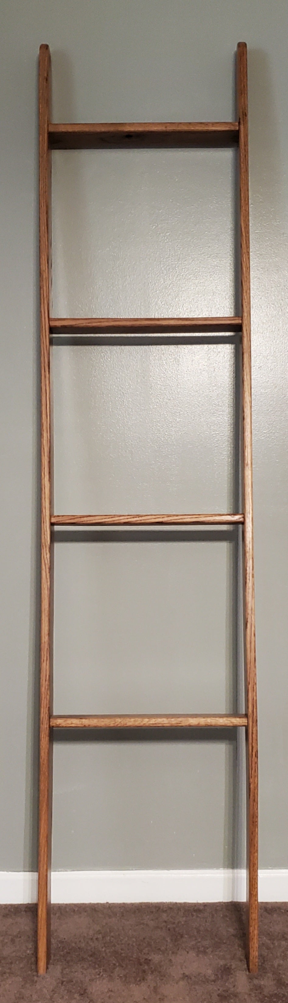 Wooden oak blanket ladder in a rich Early American stain, leaning gracefully against a plain wall. The warm, rustic finish highlights the natural grain of the oak, offering both style and functionality. Ideal for storing blankets, towels, or throws, this sturdy ladder adds a charming, vintage-inspired touch to any room.