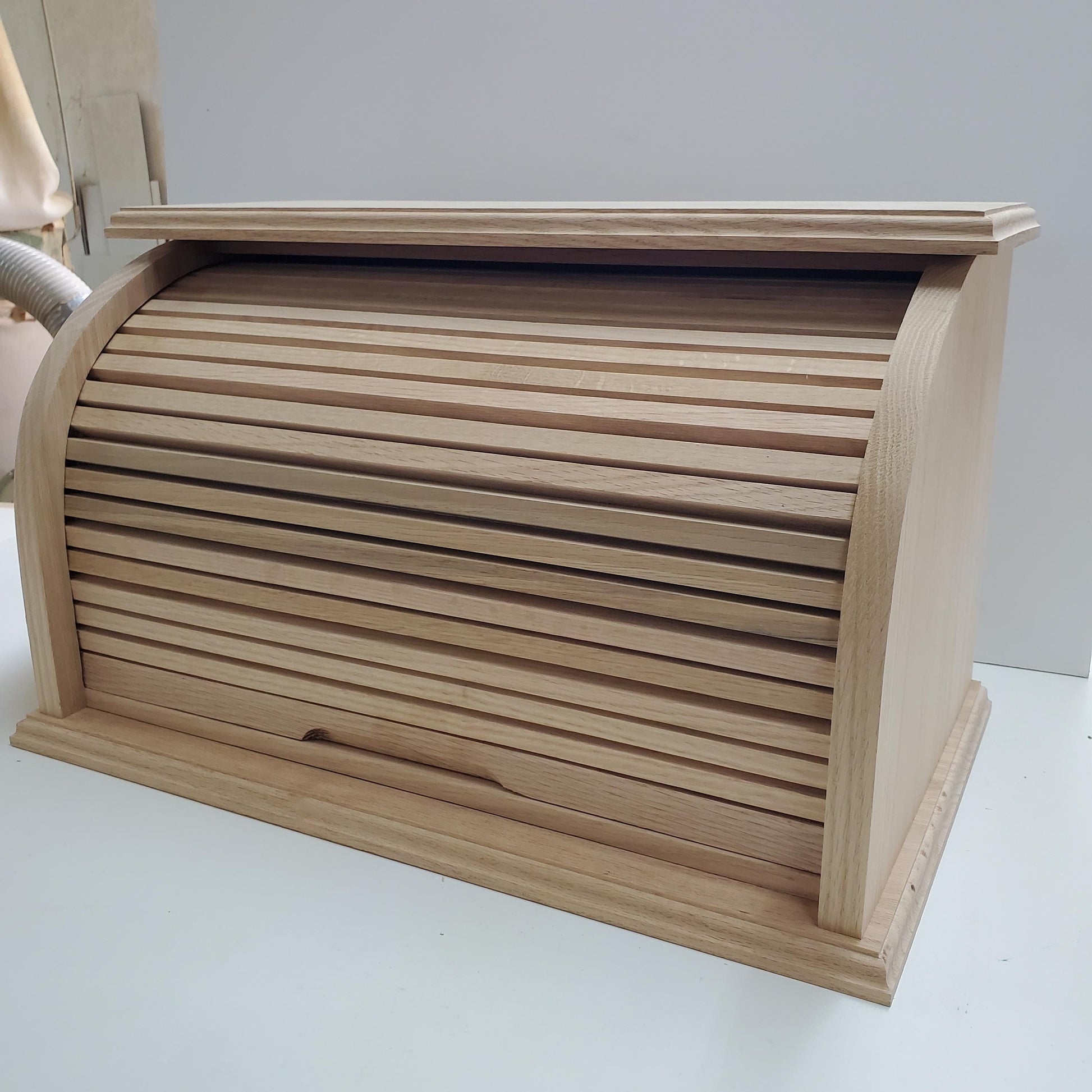 Oak bread box with a roll-top door, shown from the front. The natural oak wood showcases a beautiful grain pattern, offering both style and functionality. Perfect for keeping bread and baked goods fresh, while adding a warm, rustic charm to your kitchen. Ideal for customizing with a preferred stain to add a personal touch.