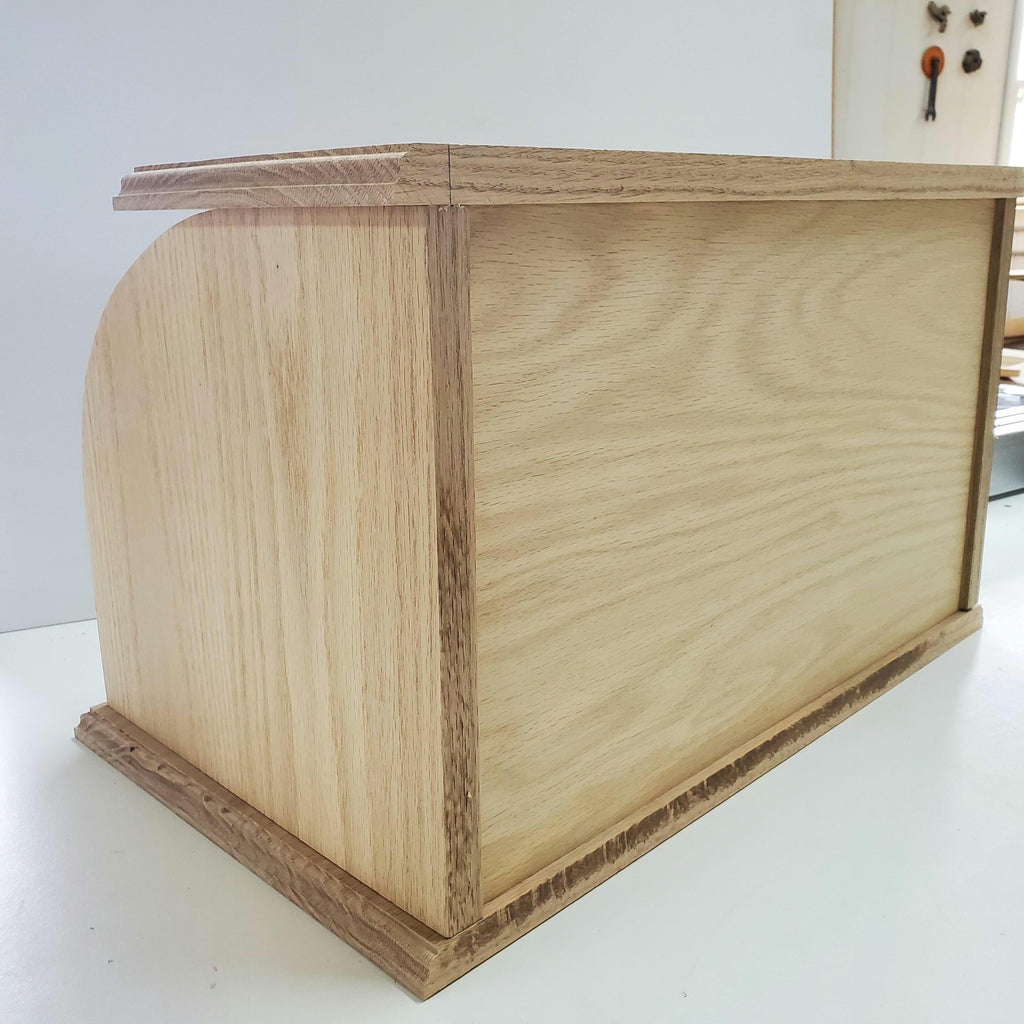 Back of Oak bread box with a roll-top door, crafted from natural oak wood that highlights the beautiful grain. The spacious interior helps keep bread and baked goods fresh, while the sturdy construction and classic design bring a warm, rustic touch to your kitchen. Perfect for customizing with your preferred stain for a personal touch.