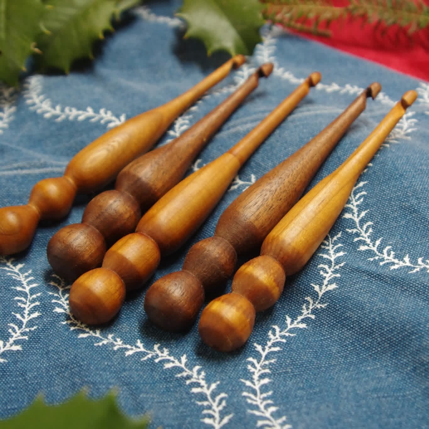 Set of wooden crochet hooks on a blue fabric background with green leaves.