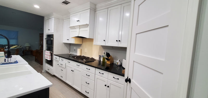 Modern kitchen with white cabinets, black countertops, and stainless steel appliances.