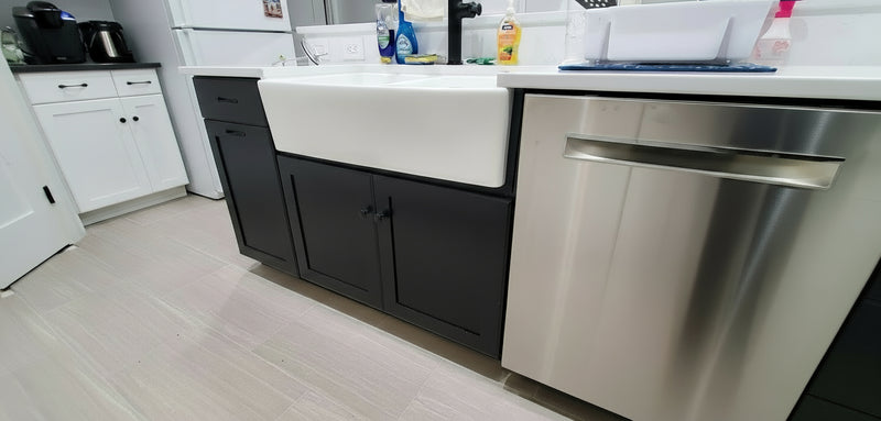 painted oak kitchen with black cabinets, white countertop, and stainless steel appliances. featuring a porcelain farm house sink and pullout for trash cans
