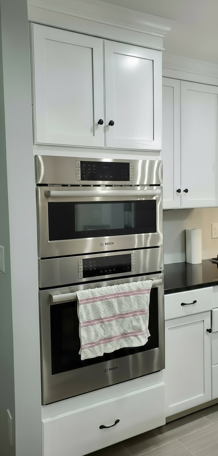 Stainless steel oven and microwave combo in a kitchen with white cabinets.